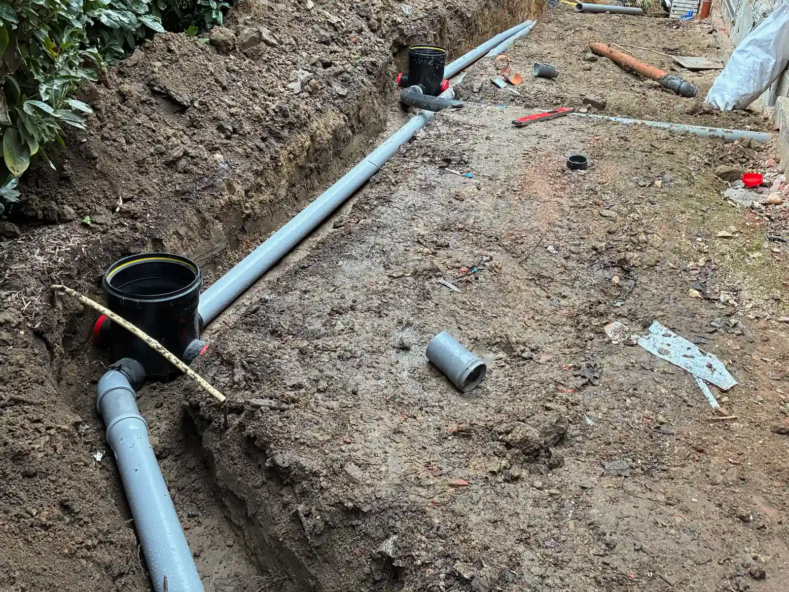 Sleuf met rioleringsbuizen en een toezichtsput langs een woning